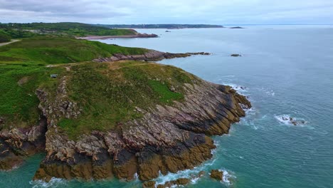 elevated drone view of rocky coastal point with geological surfaces and surrounded by clear blue seawater at pointe aux chèvres, brittany, france.