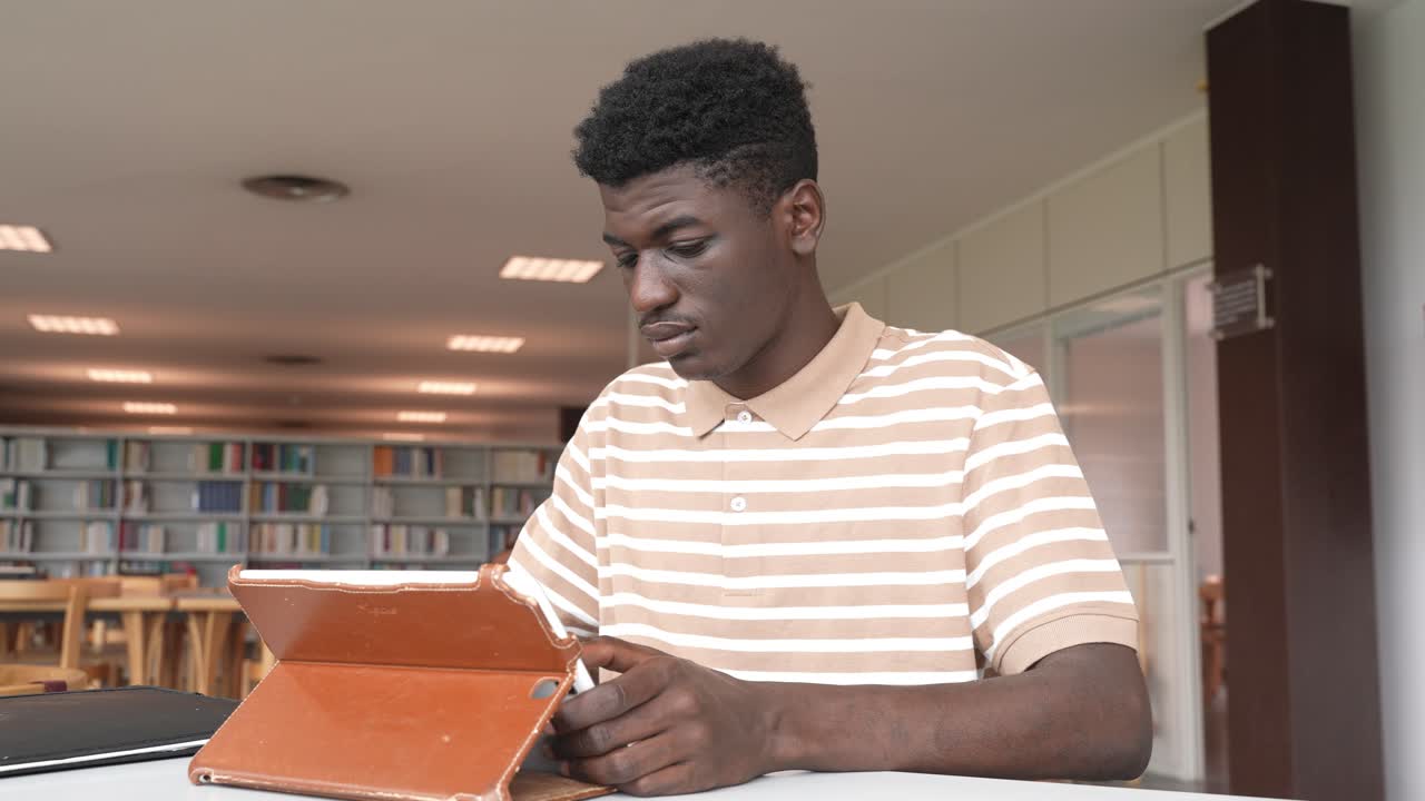 estudiante negro haciendo la tarea con una tableta en la biblioteca