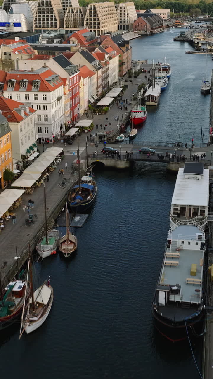 Luftfoto med drone af både på Nyhavns havnefront, kanal og underholdningsdistrikt i København, Danmark i dagslys. Lodret