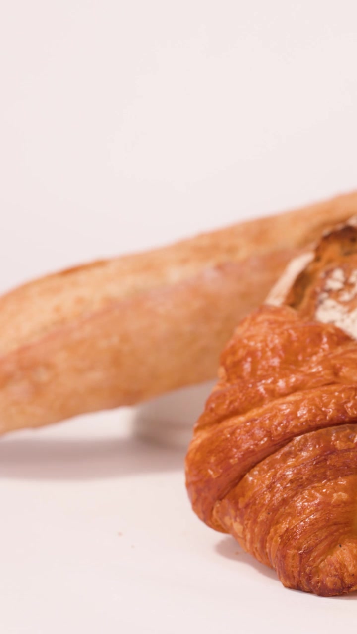 Primo piano di una mano che rimuove pane a lievitazione naturale da una selezione di croissant e baguette.