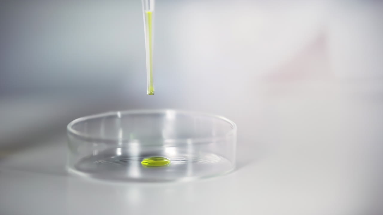 Laboratory worker scientist adding pipette dropping a colored liquid to petri dish conducting scientific experiment in lab setting. Chemistry concept for medical research and analysis