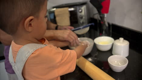 slow motion of a small mexican latin boy sifting flour on a bowl with his hands cooking with his father some cookies