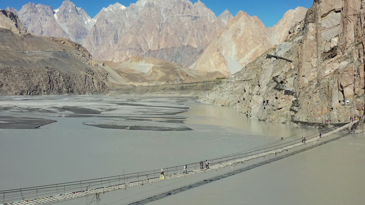 drones aéreos de turistas cruzando el famoso puente hussaini en hunza pakistán con un río rápido que fluye debajo y las montañas de conos passu en la distancia