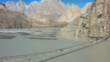 aerial drone of tourists crossing the famous hussaini bridge in hunza pakistan with a fast river flowing below and the passu cones mountains in the distance