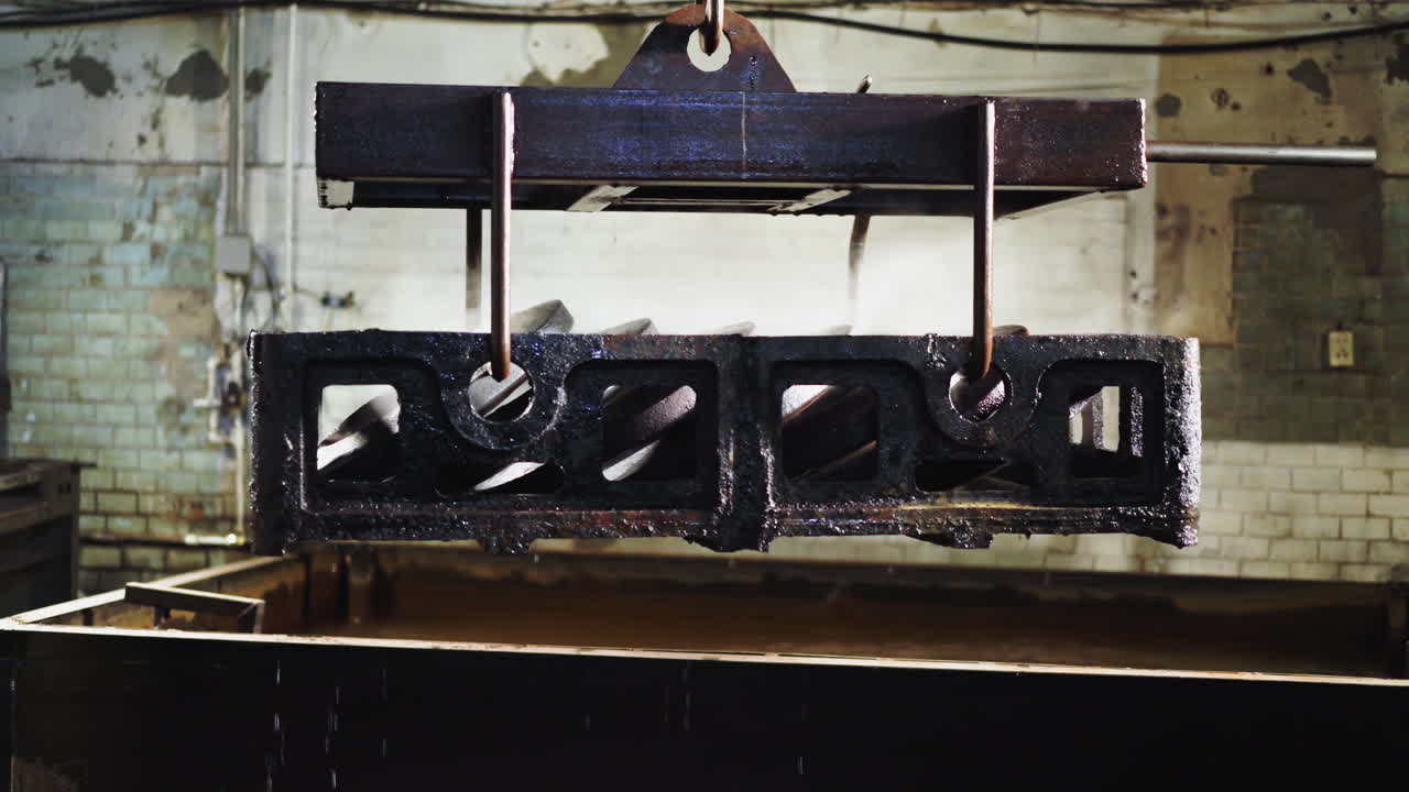 надземный кран поднимает блестящие стальные отливки из тушительной ванны в тусклой литейной фабрике, мокрые стальные литейные изделия, подвешенные на кране в промышленной литейной заводе после тушения водой