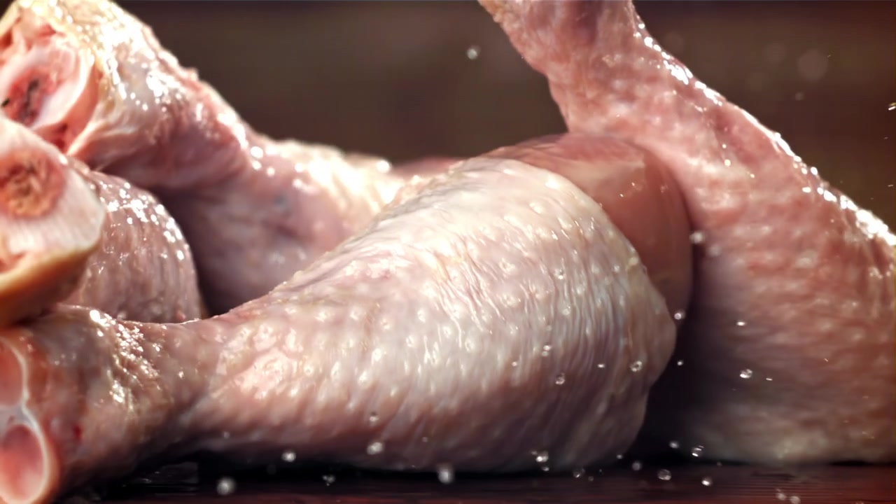 Fusi di pollo freschi e crudi che schizzano acqua al rallentatore