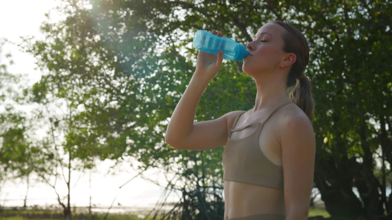 Giovane donna che beve acqua dalla bottiglia all'aperto sotto il sole