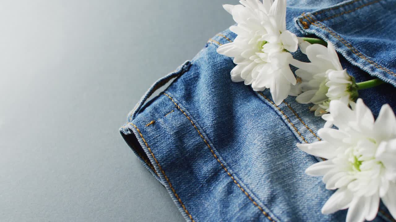 Primo piano di jeans con fiori bianchi su sfondo grigio con spazio per il testo