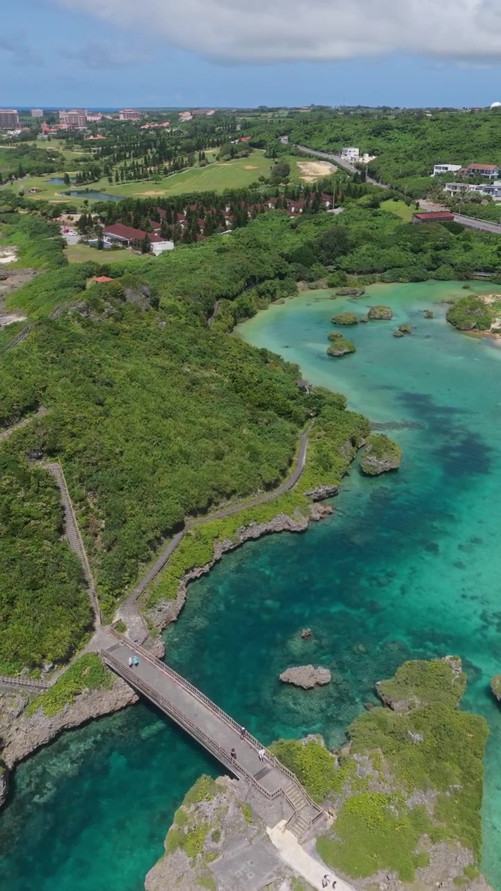 Vista aerea ravvicinata del Ponte Imgya con persone che camminano, acqua di alta marea, case ed edifici di resort vicino al Giardino Marino di Imgya, Okinawa, Giappone.