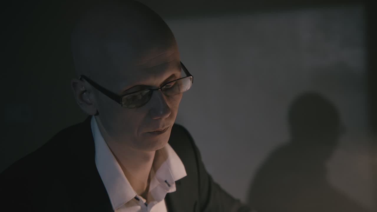 Pale bald accountant looks through the tax papers in the weird room at night