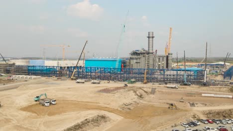 Construction-Site-with-Cranes-and-Trucks-moving-sand-building-a-factory-on-a-sunny-day-Drone-Shot-4K