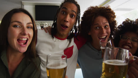 Diverse-group-of-happy-friends-watching-a-game-drinking-beers-and-taking-a-selfie-at-a-bar