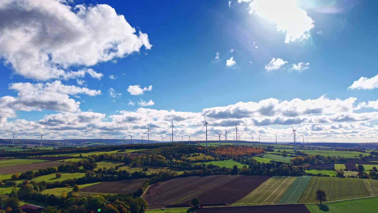 Vasti campi verdi sotto un cielo blu brillante con turbine eoliche che ruotano dolcemente in una giornata di sole in campagna