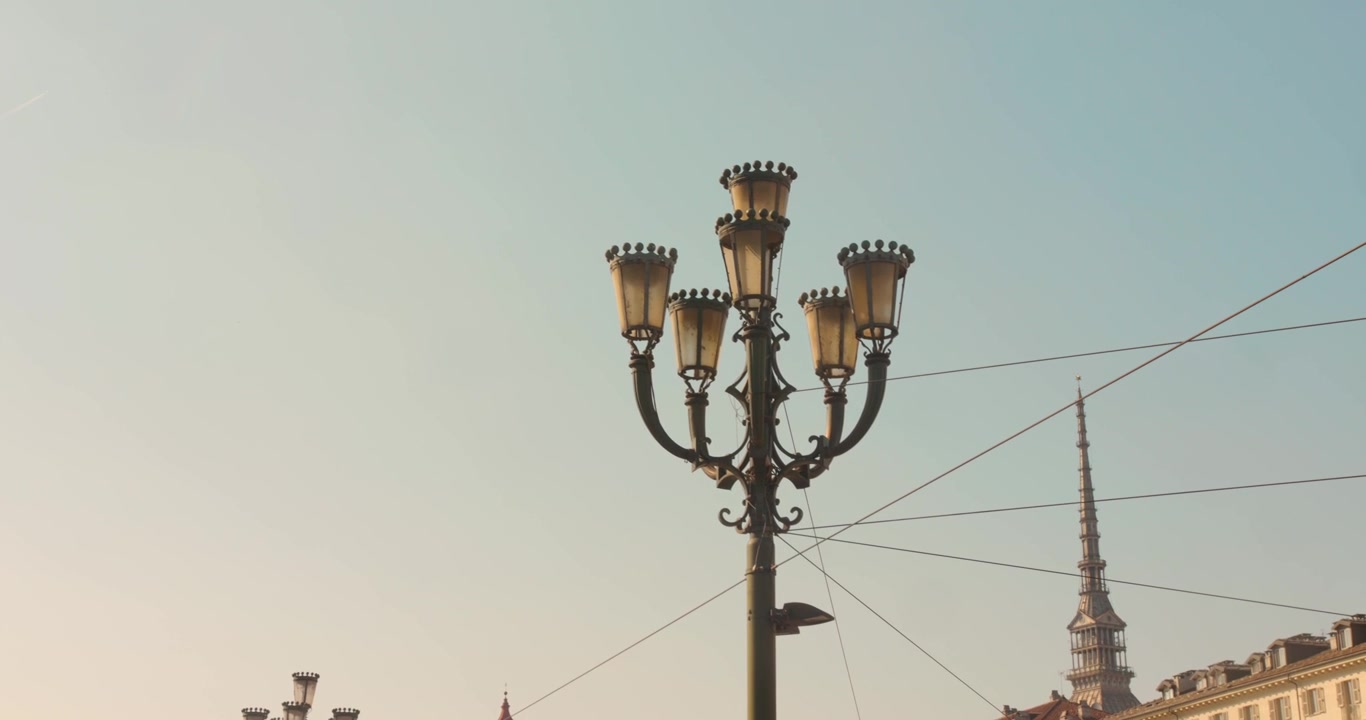 Farola histórica y elegantemente decorada con la torre Mole Antonelliana elevándose sobre el horizonte de Turín, Italia.