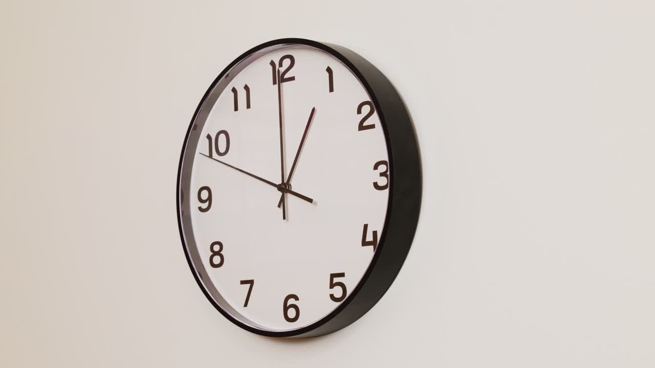A close-up 4K shot of a black and white wall clock filling the frame, showing the time as 1:00.