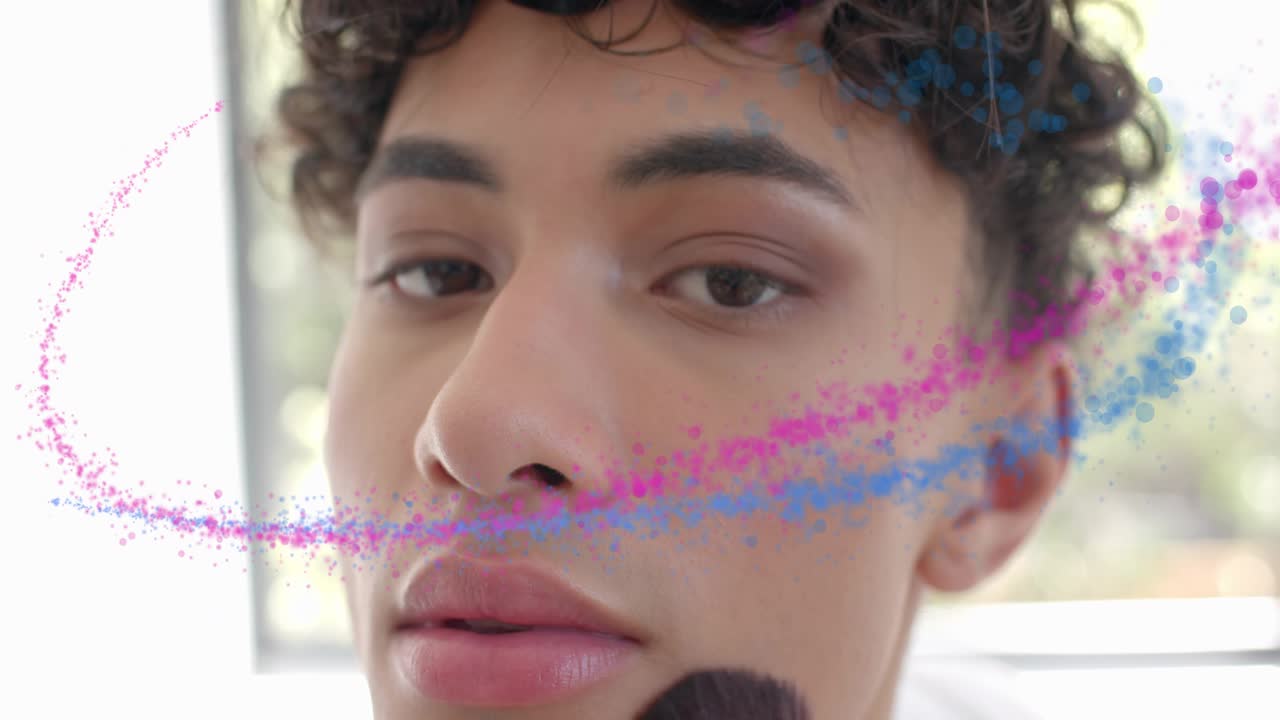 Man bringing brush to cheek, showing makeup blending while pink blue swirls partly obscuring face