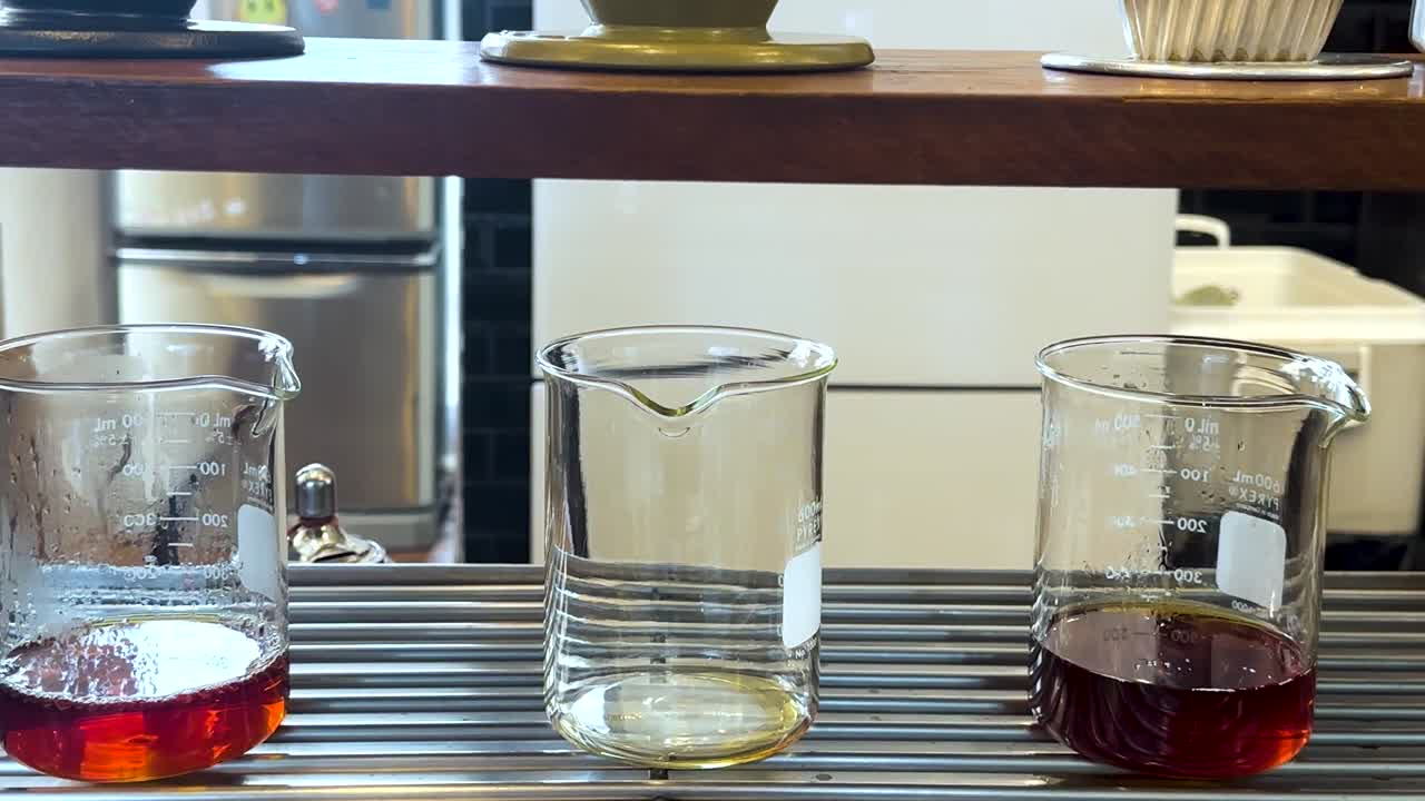 プロのコーヒー抽出プロセス中に、3つのガラス製ビーカーが金属製のラックに置かれています。