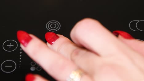 female finger operating electric stove, nicely manicured finger nails, red polish, led indicators illuminated, extreme close up