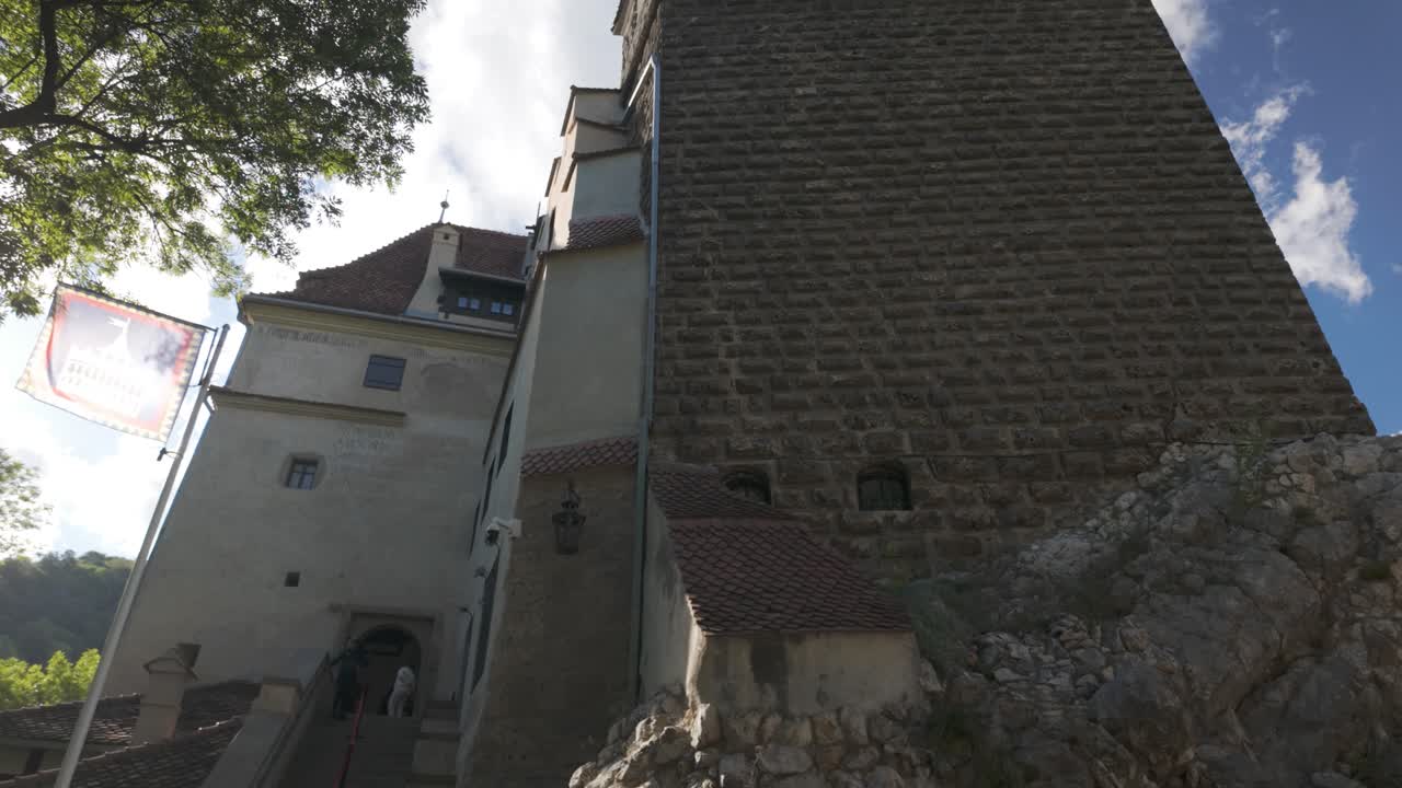 Upward pan starting at the entrance of Bran Castle, revealing its towers rising into cloudy skies