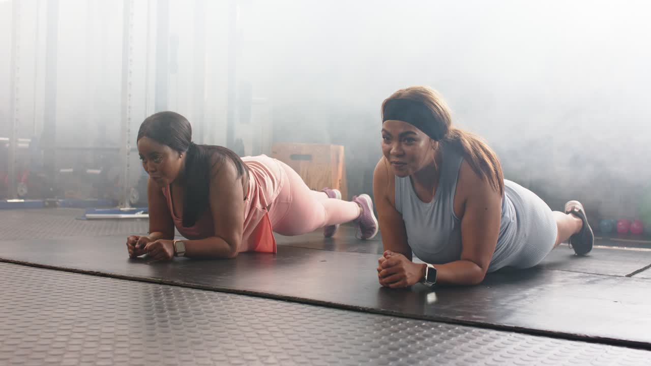 Diverse female friends responding to trainer cue, holding plank on yoga mats for core strength
