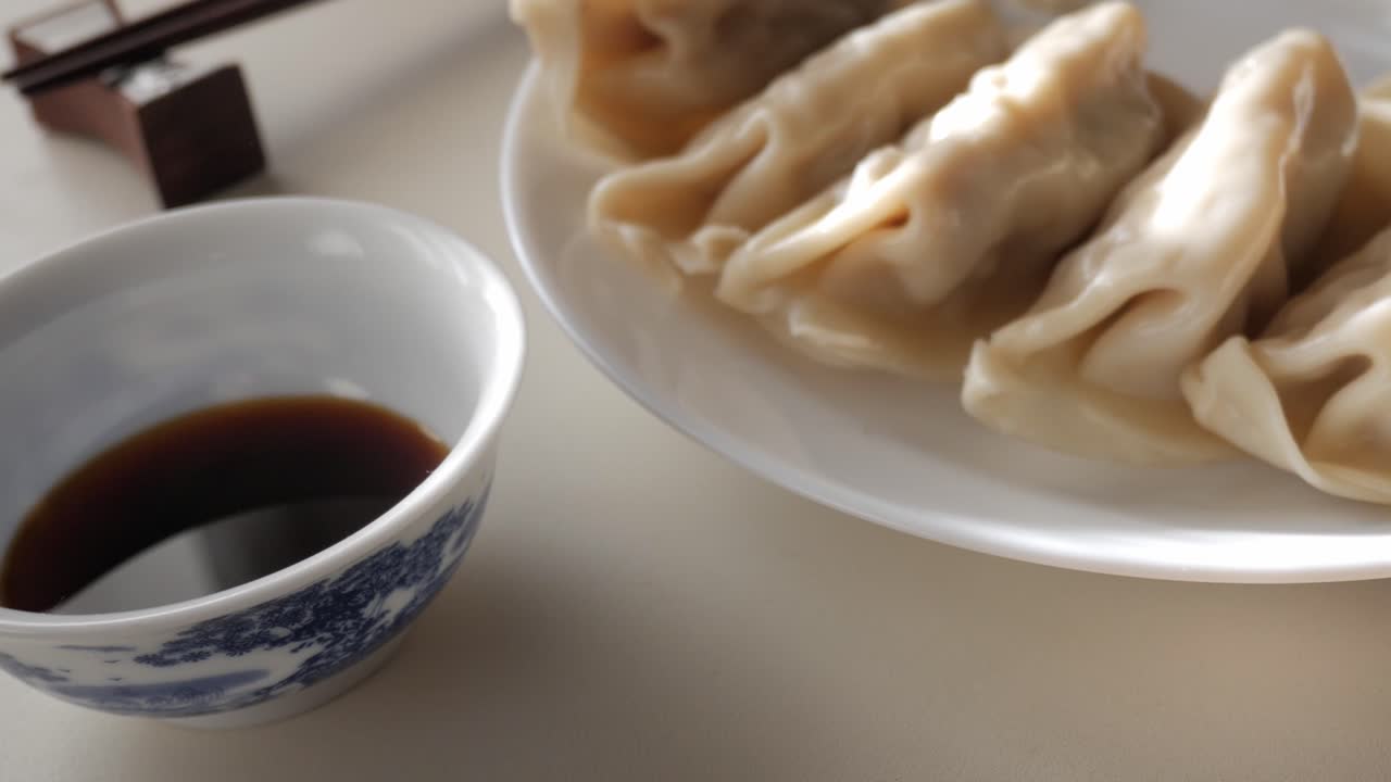 Steamed dumplings on plate, soy dipping sauce in focus, quiet and cozy setting