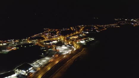 Toma-Aérea-En-órbita-Que-Muestra-La-Ciudad-De-Borgarnes-En-El-Oeste-De-Islandia-Por-La-Noche-Con-Vehículos-Conduciendo-En-La-Carretera-E-Iluminando-Edificios.