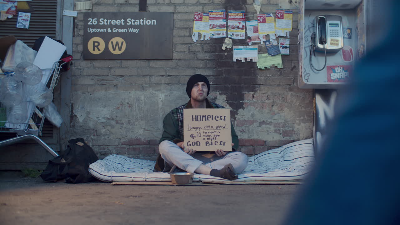 Homeless Man Begging for Money with Sign on Busy Urban Street