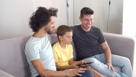 happy gay parents and son sitting together on couch