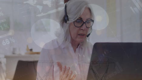 animation of financial data processing over senior caucasian woman using phone headset and laptop