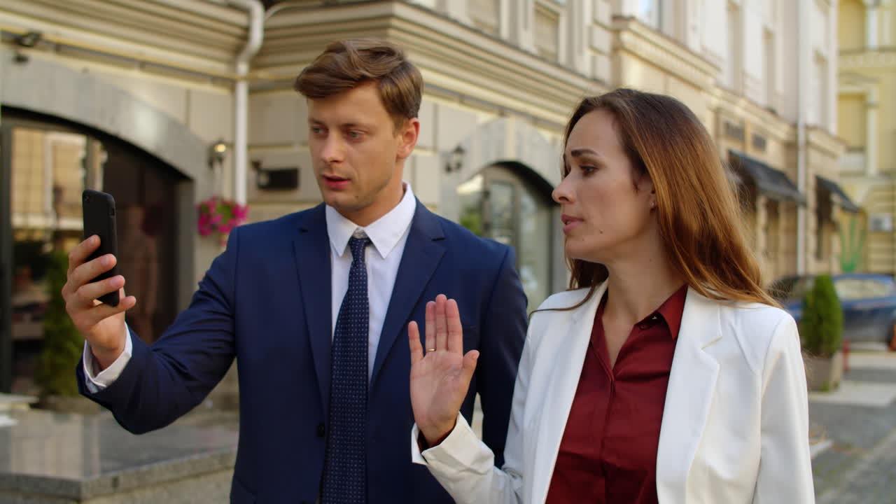серьезная деловая пара разговаривает по видеозвонку онлайн по мобильному телефону на открытом воздухе