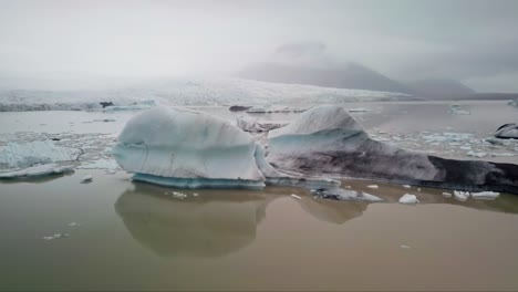 Orbiting-aerial-shot-of-iceberg-in-lagoon-with-glacier-in-the-background