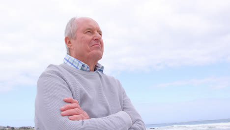 low angle view of old caucasian senior man standing with arms crossed at beach 4k