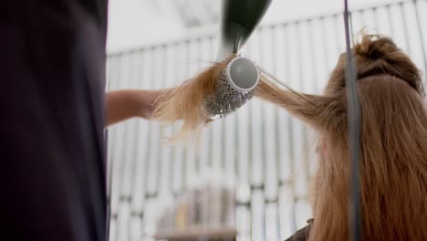 Caucasian-female-hairdresser-styling-client's-long-hair-with-hairdryer-and-brush,-in-slow-motion