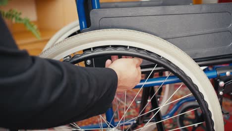 A-man-in-jeans-and-a-black-and-gray-T-shirt-checks-the-amount-of-air-in-the-tires-of-a-wheelchair