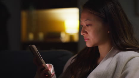 close up of woman spending evening at home sitting on sofa with mobile phone scrolling through internet or social media 4