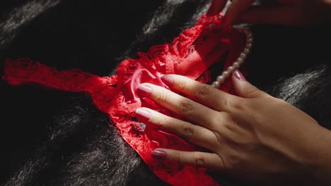 a woman's hand touches red lingerie with white pearls