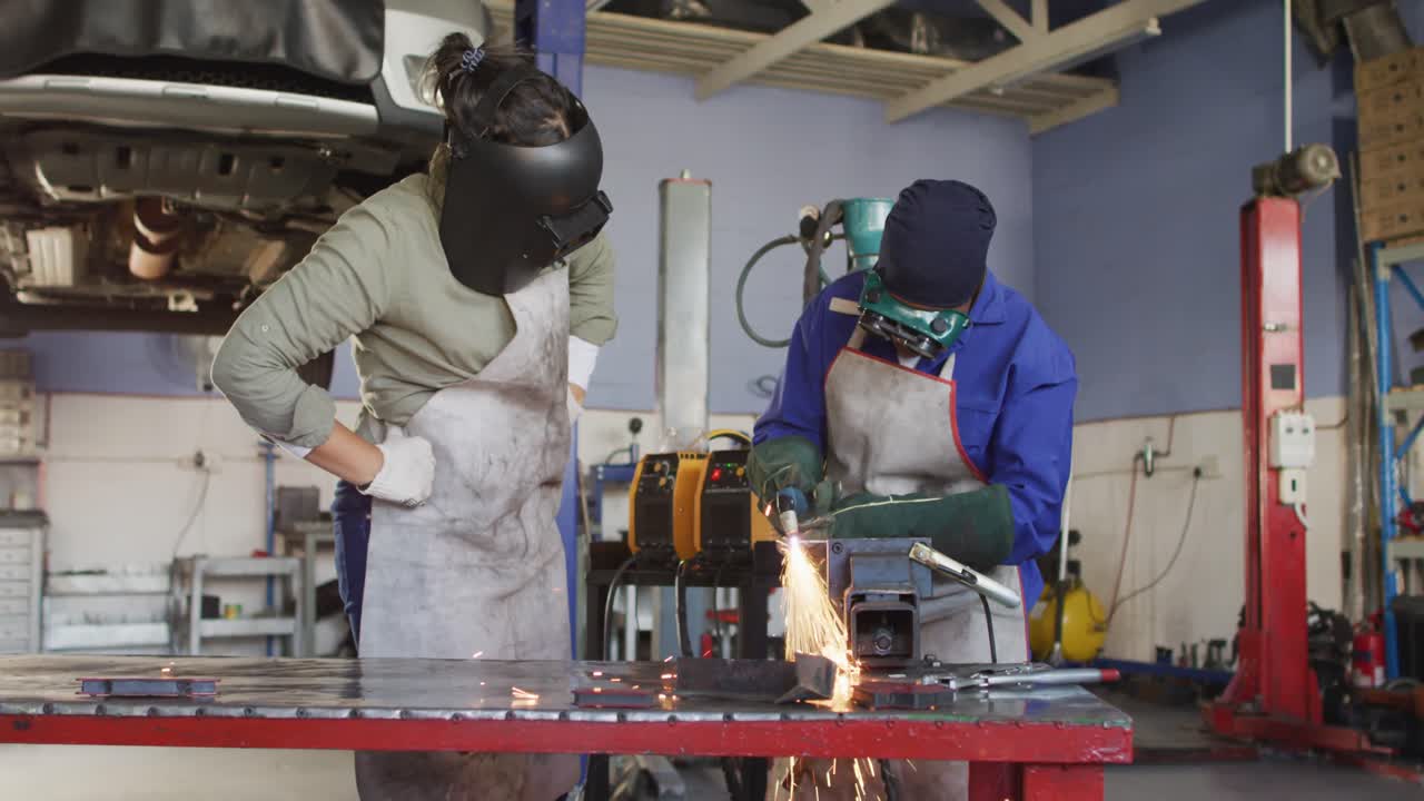 Video of two diverse female car mechanics welding and using grinder in workshop