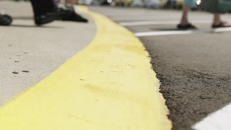 People-crossing-yellow-line-at-parking-lot,-low-angle-closeup