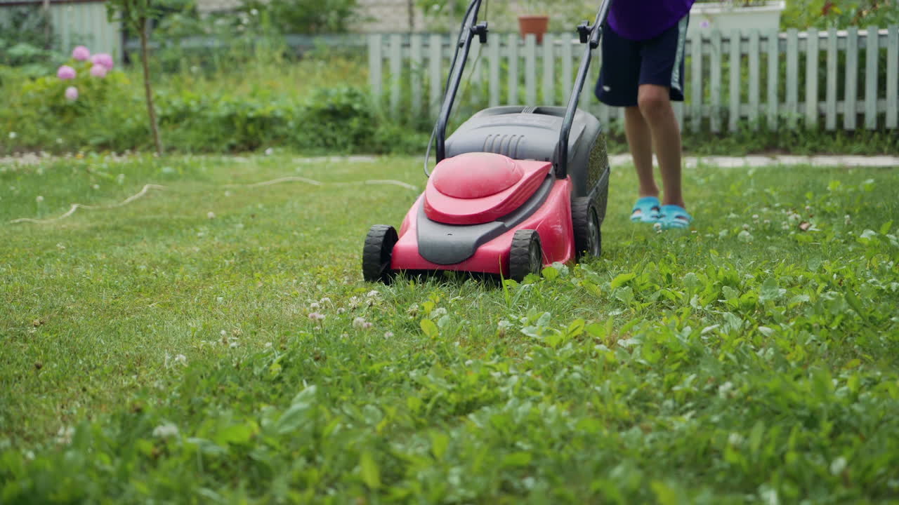 Boy running with a lawn mower in the garden. Mowing grass in the garden. Close-up