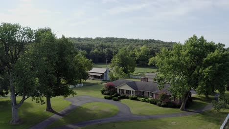 Descending-aerial-of-small-southern-farmhouse-with-forest-in-background,-4K