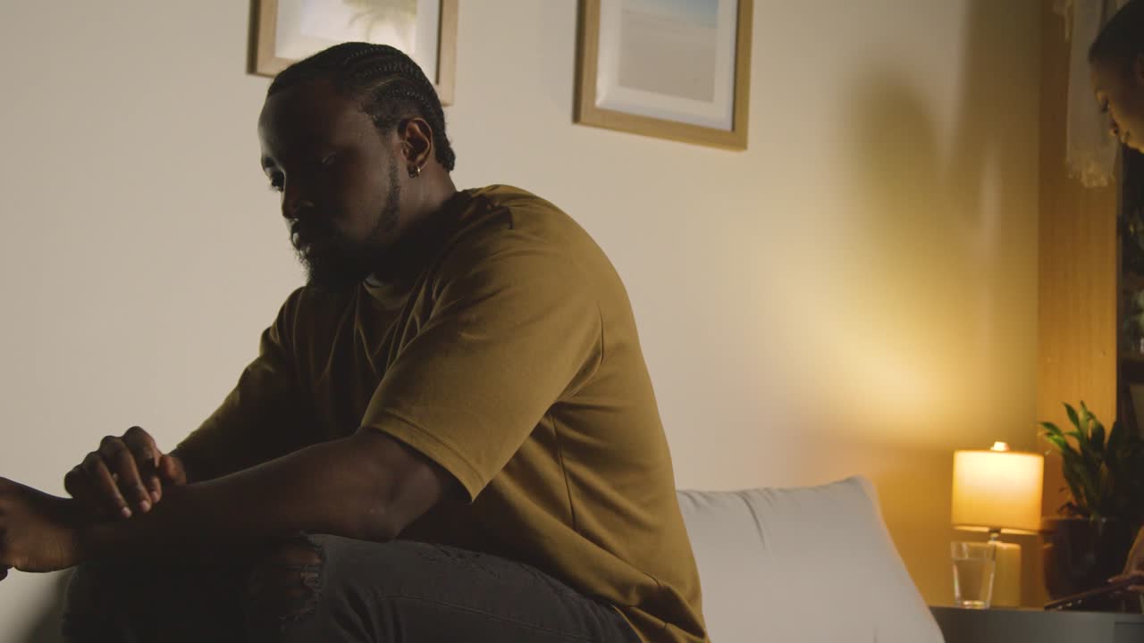 Unhappy Man Sitting On Bed At Home Is Joined By Partner Who Gives Him Hug