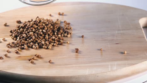 Toma-En-Cámara-Lenta-De-Semillas-De-Cilantro-Que-Se-Vierten-En-Una-Tabla-De-Madera