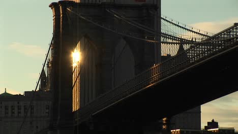 the sunlight from a building behind the brooklyn bridge shines through the infrastructure to create a lovely photo