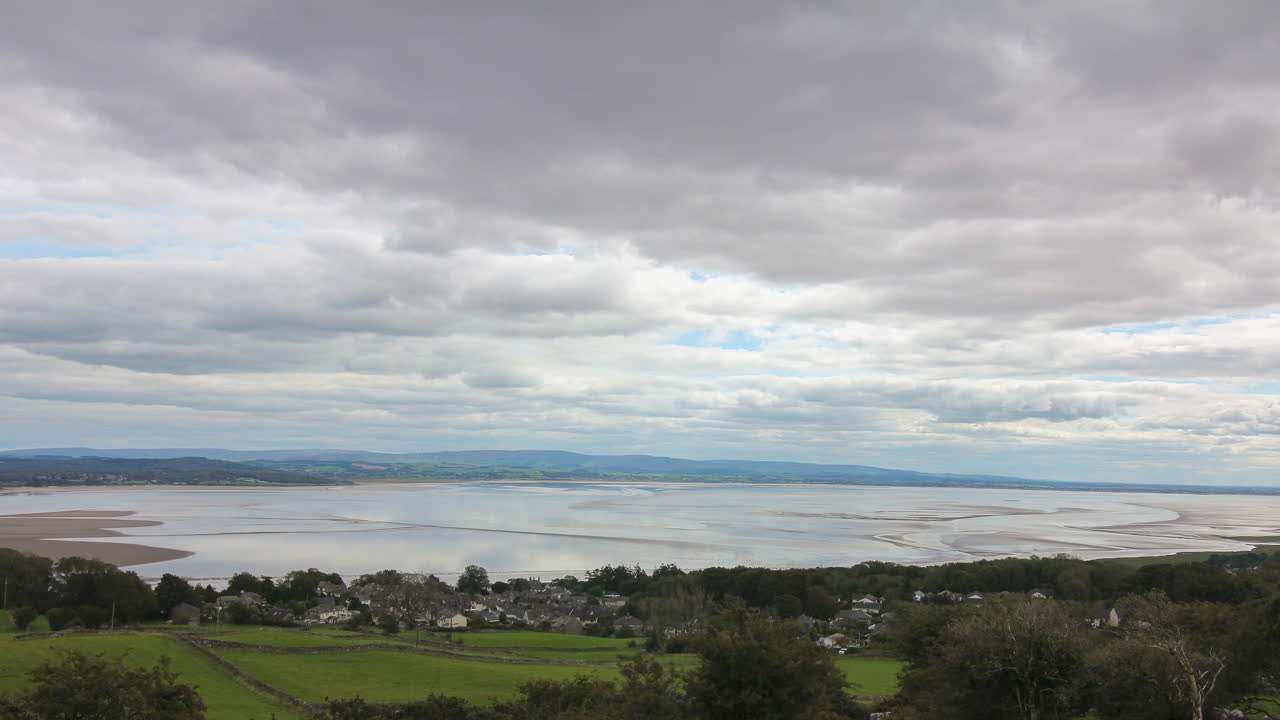 Time-lapse looking over a English costal bay with the tide receding, white clouds moving over blue sky