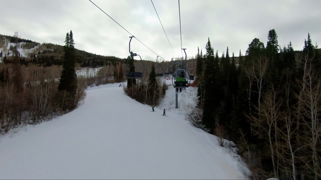 Splendido punto di vista da una seggiovia in una stazione sciistica in Colorado in una giornata invernale nuvolosa, con alti pioppi tremuli e pini che circondano piste libere con sciatori