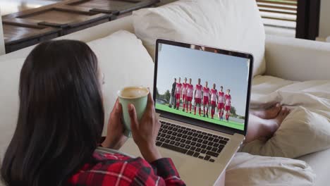compuesto de una mujer sentada en casa sosteniendo un café viendo un partido de hockey en una computadora portátil