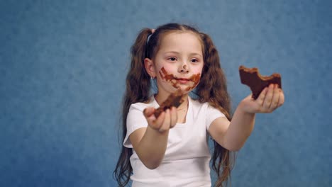 dirty face of a girl eating chocolate. two pieces of sweet chocolate in child's hands. portrait of a little kid with smeared face isolated in studio.