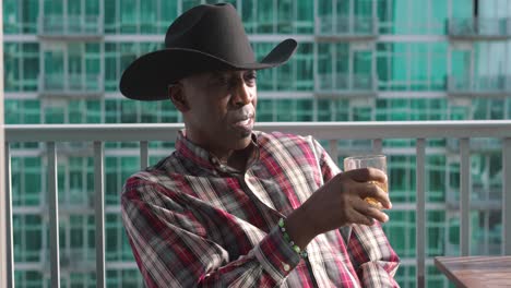 Black-man-with-cowboy-hat-with-a-glass-cup-sitting-on-balcony