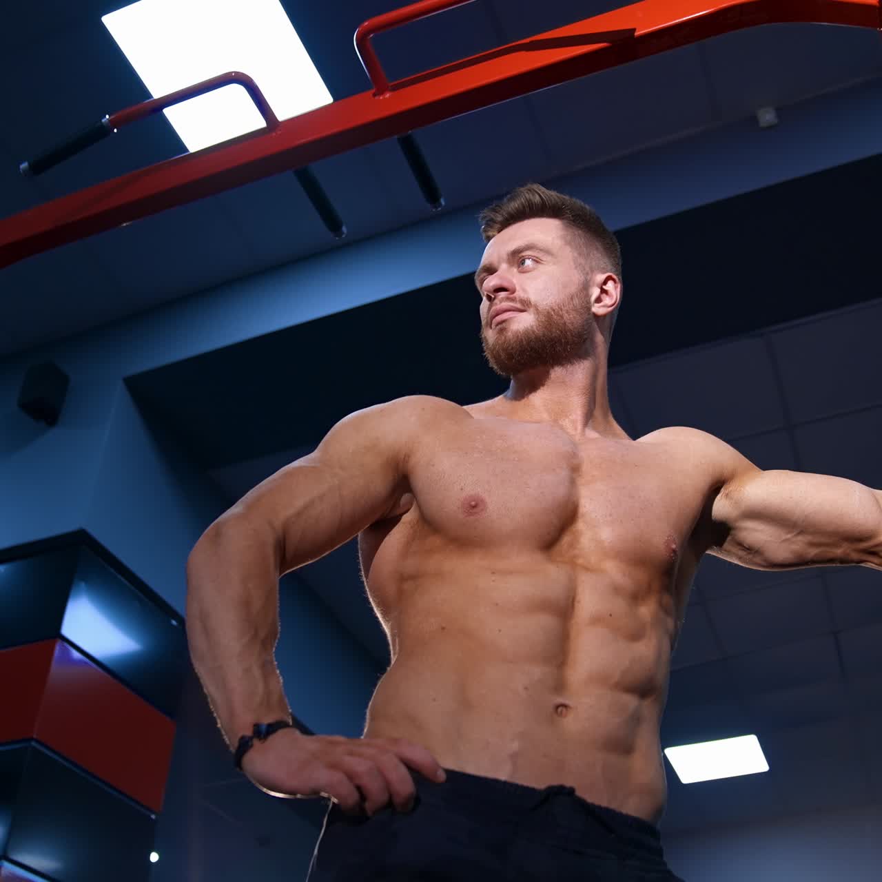 Muscular man over big gym background. Male with perfect nacked torso. Slow motion. View from below