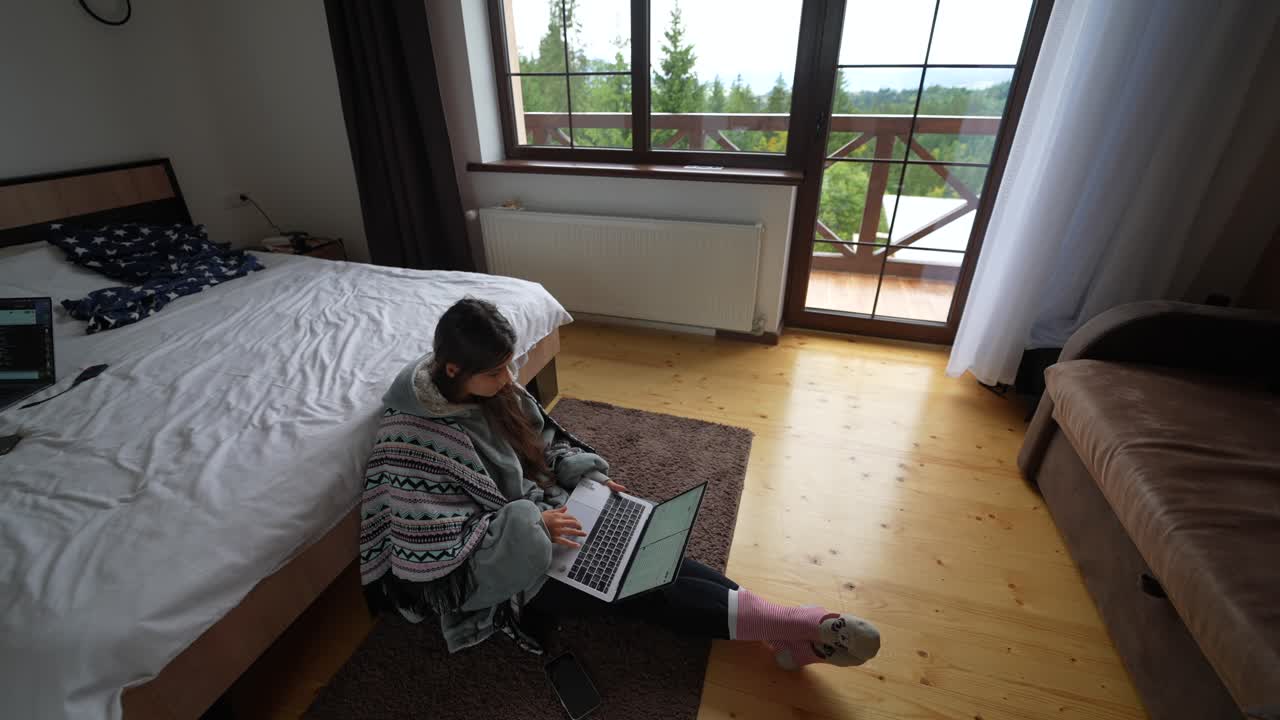 Woman working from home with a laptop in a cozy bedroom with a forest view
